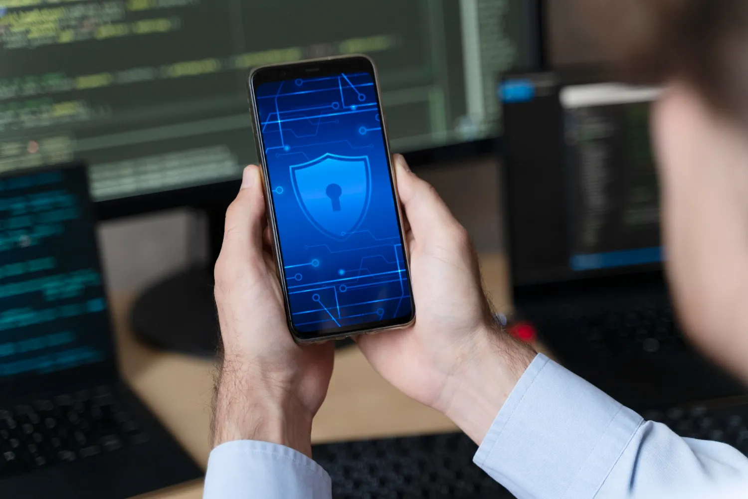 Persona sosteniendo un celular con un escudo de ciberseguridad en pantalla
